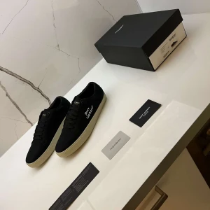 Svarta Saint Laurent sneakers strl 44 - Svarta sneakers från Saint Laurent med vit logga på sidan och guldtext på plösen och innersulan. Skorna har snörning, rund tå och vit platt sula. Tillverkade i canvas och skinn för en clean och stilren look. Kommer med originalkartong och kort. Skriv för frågor!