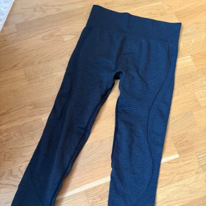 Svarta seamless leggings i M - Säljer ett par svarta seamless leggings med hög midja och snygga ribbade detaljer längs benen. Materialet är en mix av nylon, polyester och elastan som ger bra stretch och passform. Perfekta för träning eller chill. Ventilerande partier på benen för extra komfort.