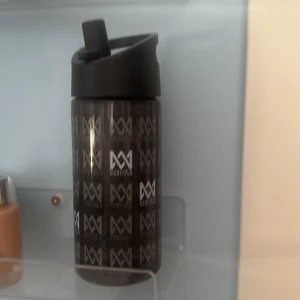 Marcus & Martinus Vattenflaska - Snygg svart vattenflaska med Marcus & Martinus-logga. Praktiskt lock med drickpip. Flaskan är använd men i gott skick, dock syns visst slitage på locket. Perfekt för fans eller till träning och vardag.