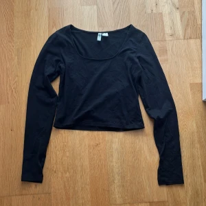 Svart långärmad topp från H&M Divided - En svart, croppad långärmad topp från H&M Divided med rundad, djup urringning. Enkel och stilren design i mjuk bomull, perfekt att matcha med jeans eller kjol. Säljes i storlek S.