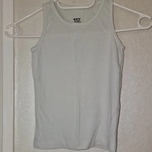 Vit linnetopp från lager 157 - En klassisk vit linnetopp från lager 157 i storlek 110. Tillverkad i 100% ekologisk bomull med rund halsringning och ärmlös design. Perfekt för en enkel och clean look, lätt att matcha med allt.