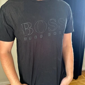 Svart Hugo Boss t-shirt med logga - Svart t-shirt från Hugo Boss med stor, diskret logga framtill och mindre logga i nacken. Klassisk rund hals och korta ärmar. Tillverkad i mjuk bomull för en skön känsla och snygg passform.