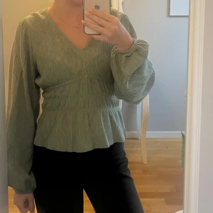 Grön v-ringad blus från Lindex - Säljer en ljusgrön blus från Lindex med v-ringning och långa puffiga ärmar. Blusen har en smockad midja och lätt rynkad struktur i tyget.  Perfekt att styla med både jeans och kjol. Storlek xs men passar också s. Använd någon enstaka gång!