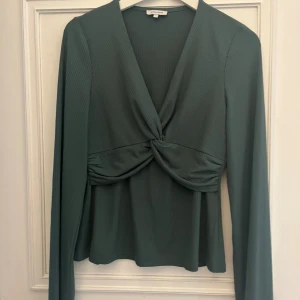 Grön omlottopp från Bubbleroom - Säljer en snygg grön omlottopp från Bubbleroom i ribbat material. Toppen har lång ärm, twistad detalj framtill och djup v-ringning. Perfekt för dig som gillar trendiga och stilrena plagg med det lilla extra.