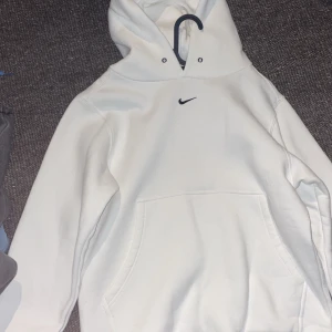 Vit hoodie från Nike med huva - Säljer en stilren vit hoodie från Nike med klassisk svart swoosh-logga på bröstet. Tröjan har huva med dragsko och en stor magficka framtill. Perfekt för en avslappnad och sportig look. Lik den förra svarta på min profil gå in och kolla där för detta var dålig bild men ocksp helt oanvänd