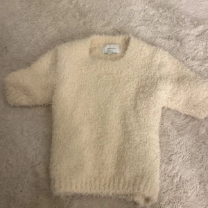 Beige fluffig stickad tröja New Edition - Supermjuk och fluffig beige stickad tröja från New Edition. Tröjan har korta ärmar och en mysig, lurvig textur som är perfekt inför höst+vintern!