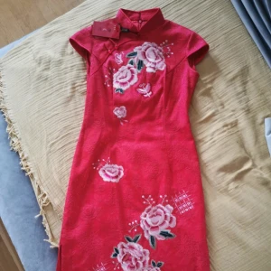 Knälång fodrad qipao från kina - Ny med taggar. Storlek M men passar även S då asiatiska storlekar är lite mindre generellt. Jättefin kinesisk röd färg med fina broderade detaljer. 