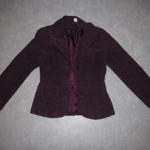 Mörk lila jacka h&m 32 - Vår-/höstjacka i härlig lila färg. Sitter tajt och snyggt. Knappar o fickor i fram. Glansigt tyg på insidan. Mycket fint skick.
