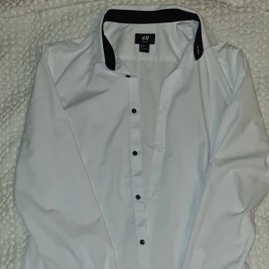 Vit skjorta stl m i nyskick. - Skjorta vit med svarta knappar köpt på H&M i storlek medium. Säljes p.ga för liten.   Använd 2 gånger.   Fläckfritt djur samt rökfritt.