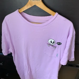 Coolshirtz tröja med ett litet skelett i fikan! I XL (extra large)  - En lila tröja, med ett litet skelett som sticker upp ur fickan! Från Coolshirtz 