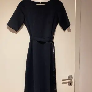 Mörkblå klänning med avtagbart skärp från Holly Whyte Lindex.  Storlek S.   I mycket bra skick, bara använd en gång.   82 % polyester, 13 % viskos, 5 % elastan. 