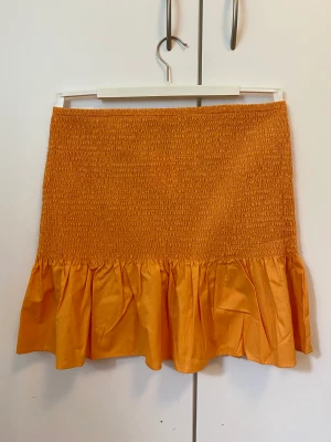 Orange kjol med smock - Aldrig använt. 38,5cm bred midja. 43cm lång. Stelt / Styvt material.