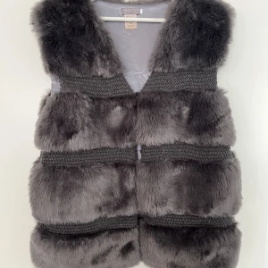 Fauxfur väst - Obs inte äkta päls! Pälsen är konstgjord men ser inte fake ut. Använd 2 gånger. Jättefint skick, endast 1 liten slitning vid insidan som går att se på sista bilden. Syns ej när västen är på. Den går att knäppa med 2 knappar (bild 1).