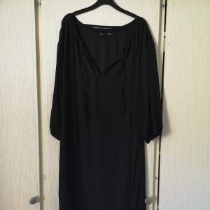 Helt ny oanvänd klänning i svart. Med snöre framtill, töjbara armar nertill, slits på båda sidor. Luftig o rymlig 