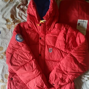 Fjällräven jacka - Röd fjällräven jacka. Från den äldre modellen 1974 expeditions serien, men i förnyad version. Finns även en smidig "gympapåse" som man får till om man kanske blir för varm. Inga fel på den. Jättefint skick. 