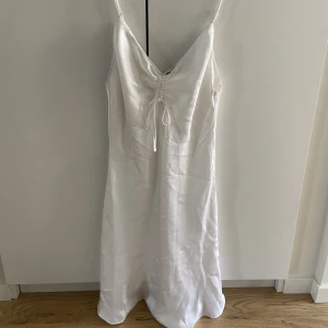 Vit klänning - Vit klänning i satin från BIKBOK i storlek S. Oanvänd med prislappen kvar