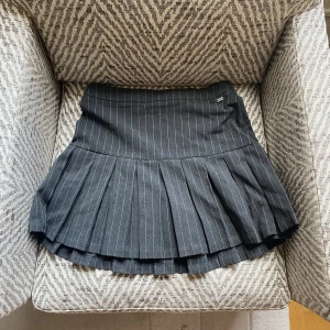 Plisserad kjol - Grå, randig kort kjol från Pull&bear. Storlek S, midjemått 33cm tvärs över. Använd enbart en eller två gånger. Dragkedja på sidan