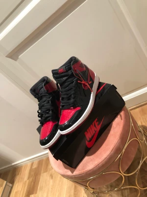 Jordan 1 high patent bred - Strlk 43, små repor på sidorna av båda skorna. Box oskadad, båda snörerna ingår(röd&svart) och allt annat. Skick 7/10 svårt att inte få repor eftersom det är ett annat slags material än andra Jordan 1
