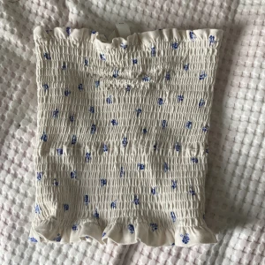 Bandå topp - Säljer denna vit/blommiga toppen från hm. Den är i nyskick och har aldrig använt (bara när jag tagit bild till denna annons), toppen har heller inga defekter💓