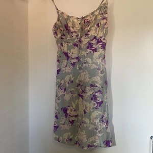 Blommig klänning med prislapp kvar - Ej använd (prislapp kvar). Går ner halvvägs till knäna på mig som är 166 cm. Så fin över bysten med rysch som går att dra åt. Köpare står frakt.
