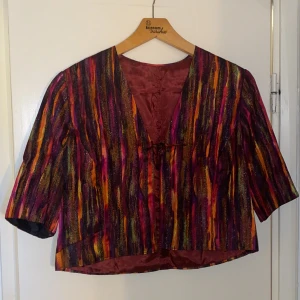 Glittrig överdel - Jättefint loppisfynd! En glittrig kavajliknande överdel i vackera färger. Slutar i midjan men är stor och luftig. 