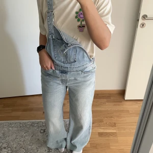 Hängselbyxor - jeans - Ett par ljusblåa hängselbyxor från Zara i storlek M🙏🏼 Helt oanvända och har en mörkblå detalj på ena bakfickan, köptes för ca 799kr 🥳 Sjukt sköna, har en rak modell i benen och är långa!
