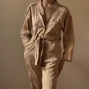 Rachel Comey made in New York tan jumpsuit 1 chest pocket  2side frontal pockets 2back flap pockets  button down opening, waist strap Rachel Comey Buttons 2 minor stains one in the front, one in back not visible when worn  size XS