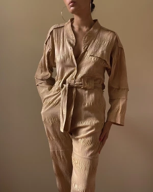 Preloved Rachel Comey Silk Blend Jumpsuit - Rachel Comey made in New York tan jumpsuit 1 chest pocket  2side frontal pockets 2back flap pockets  button down opening, waist strap Rachel Comey Buttons 2 minor stains one in the front, one in back not visible when worn  size XS