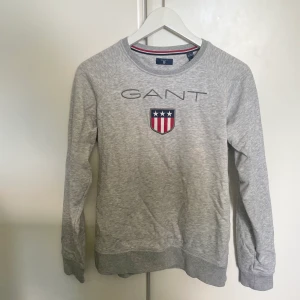 Grå Gant Tröja - En grå Gant tröja i storlek 158/164. Är i mycket bra skick men har svaga gräsfläckar på ena ärmen. Priset går att diskutera ❤️Nypris: 700kr