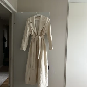 Vit trenchcoat  - Vit trenchoat som aldrig använts. Har knappar för att knäppa på päls. Är liten i storleken. 