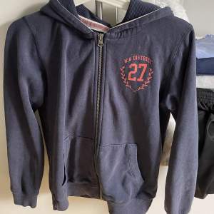 En mörkblå zip-upp hoddie med ett rosa tryck från märket warp i storlek 158/164