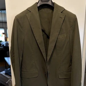 Oscar Jacobsson  - Snygg Blazer från Oscar Jacobsson! Kavajen är i fint skick, i storlek: 48. En snygg färg, lite olivgrön. Stygnen runt b.la. Kavajslagen ger en avslappnad look, så den passar perfekt till jeans t.ex. Passformen är riktigt bra. Men eventuellt korta ärmarna.