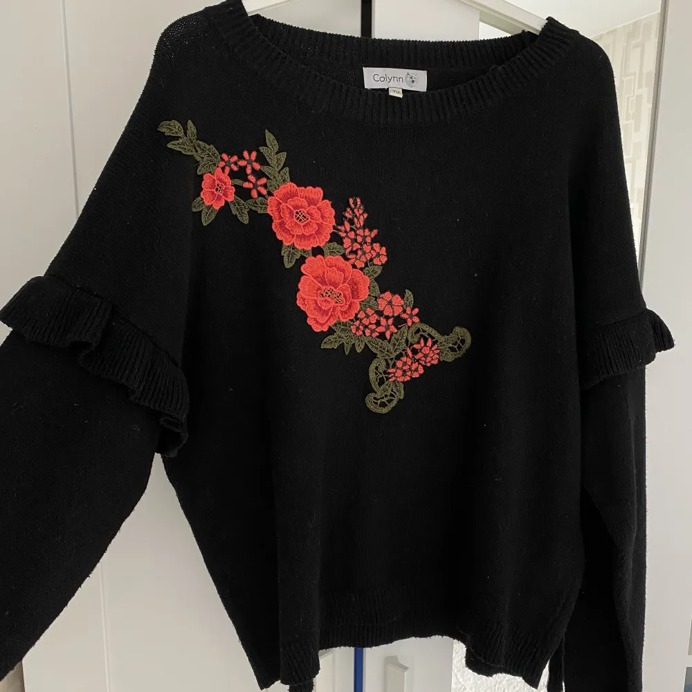 En svart tröja med blommor som tryck på tröjan. Har även detaljer på ärmarna.. Stickat.
