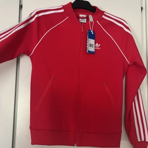 Adidas kofta - Röd adidas kofta köpt på Zalando i strl 32 men passar även 34 alla lappar är kvar då den aldrig är använd