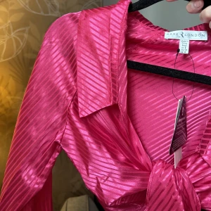 Rosa-randig knyttopp - Somrig topp man knyter i fram, skönt material. Oanvänd och endast testad! Lyser så fint rosa om den!