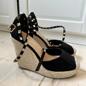 Valentino inspirerade klackar - Ursnygga kilklackar i svart mocka med gulddetaljer! Valentino inspirerade, ca 10cm hög klack. Bandet som spänns fast vid vristen viras runt smalbenet. Köpta i Italien för 800kr, säljs för 150kr. Klackarn är sparsamt använda🇮🇹✨