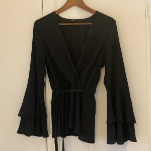 Svart blus - Svart v-ringad topp. Knytning i midjan. Vida ärmar. Stl 38/40 eller Medium