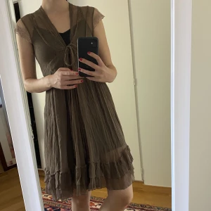 Brun/beige klänning - Tunn brun klänning, perfekt över badkläder på stranden eller med en underklänning då den är ganska genomsiktlig. Gulliga blommor på axeln/armen. Saknar lapp så uppskattad storlek, passar mig som har S. 