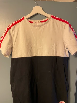 Två färgad tisha - T shirt. Mörkblå i båtten vit i toppen. Röd på axlarna 