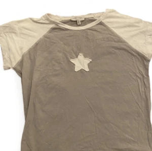 T-Shirt med stjärna - Köpt från Pull&bear i somras, använd endast en gång. Säljer då den inte riktigt är min stil längre. Jätte fint skick. Färgen är grå-beige och vit !