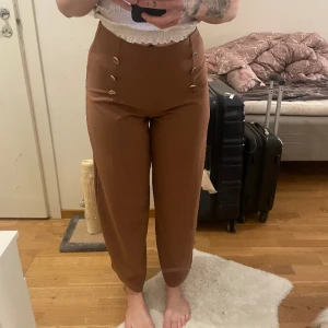 Kostymbyxor - Vida i benen Kostymbyxor från Primark, storlek EUR 36, passar nog även M. Guld detaljer ”knappar” Färgen på byxorna är rödbrun