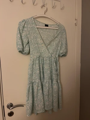 Grön blommig klänning från Gina trocot  - Det är ingen fläk längst upp på baksidan den är den svarta lappen som gör så att det blir så.💓 finns Spännband i midjan , säljer för den är för kort.