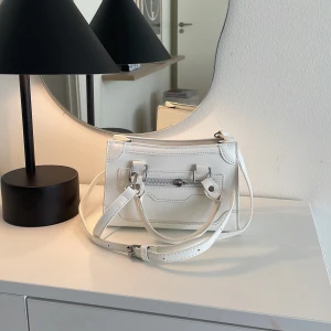 Vit Liten Väska - Vit liten väska. De små handtagen på dragkedjorna har försvunnit men funkar att öppna ändå. Söt att ha med ut!