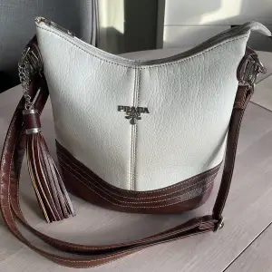 Säljer en cremevit handväska med bruna detaljer och avtagbar axelrem, Prada (kopia)