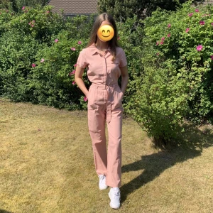 Rosa jumpsuit - Rosa jumpsuit från Hollister, krage, bröstficka, skärp och två fickor, använd 1-2 gånger
