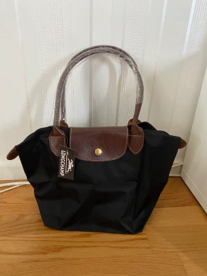 Longchamp tote, M - ”Le Pliage”, M. Inköpt på longchamp.com  Nylon och läder.  Prislapp och skyddsplast kvar. Nypris: 1350kr  https://www.longchamp.com/se/en/products/tote-bag-m-L2605089001.html 