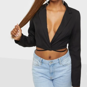 Svart top från Nelly - Säljer denna svarta top, aldrig använd. Endast provad.  Med en liten knytning ner till. Materialet är kostym material🤎  Nypris: 449:-