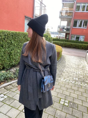 Grå kappa från Wera Stockholm - Grå höstkappa från Wera Stockholm. Stängs omlott och med ett knytskärp.   Nypris: 1199:-  80% ull 20% polyamid