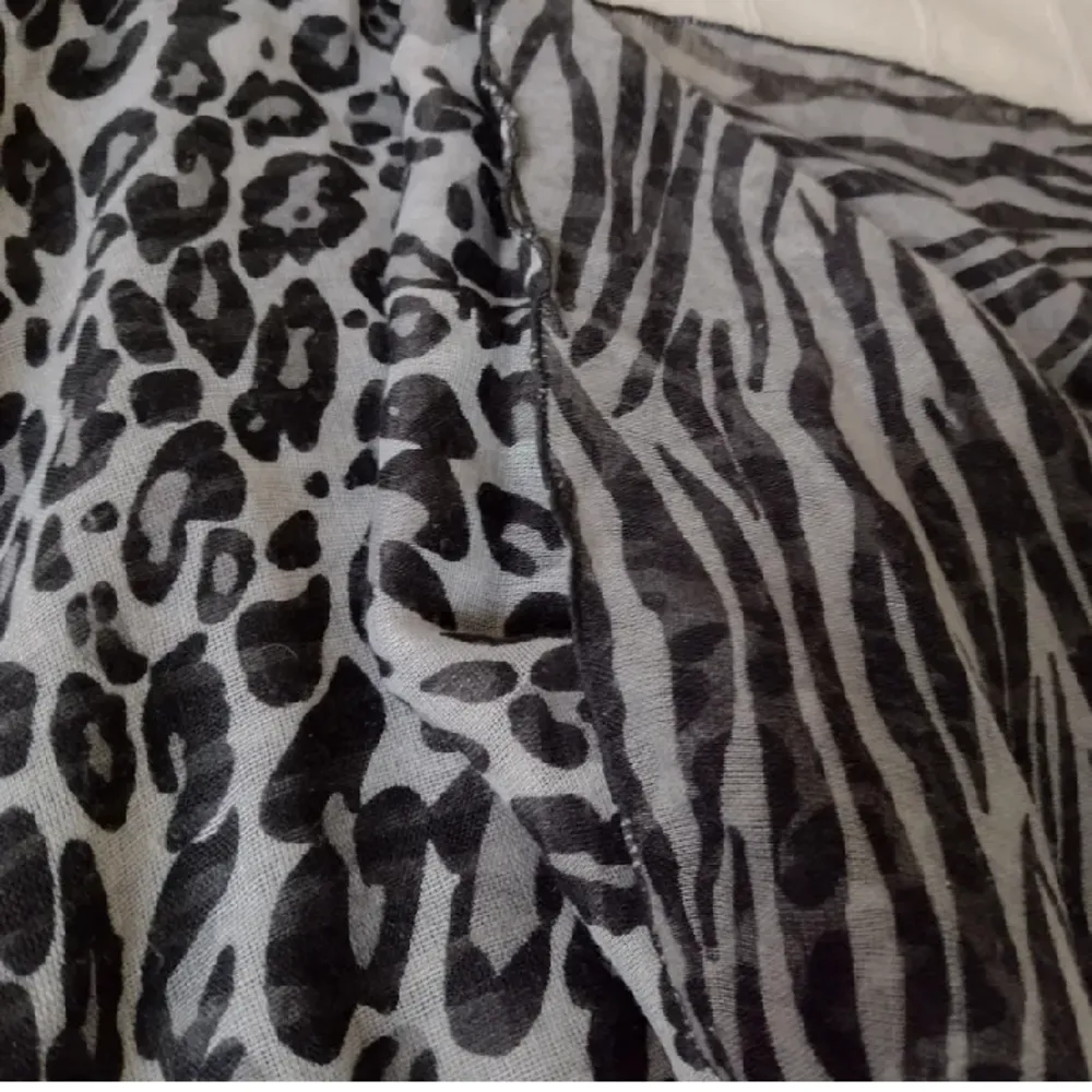 Lång grå/svart djurmönstrad sjal. Olika mönster på fram- och baksida. Nästan 2 m lång och 70 cm bred. En del dragna trådar. Tunn och lätt.. Övrigt.