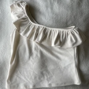 Topp - Säljer denna as fina topp från H&M som är superskön och har en jättefin volang längs ärmen! Den är one shoulder💗